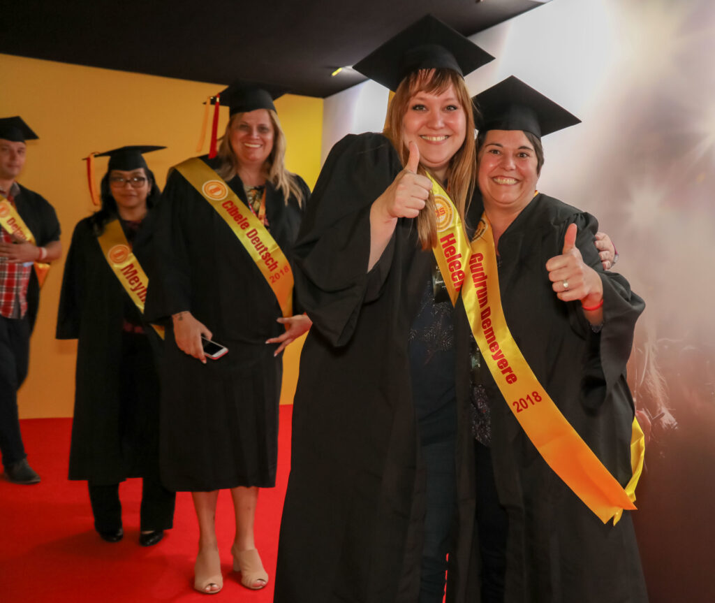 Picture of people in caps and gowns smiling with thumbs up