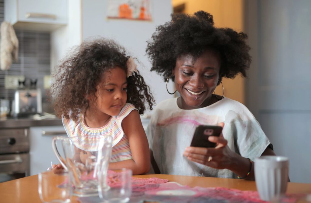A picture of a child on their mothers lap both looking at a mobile phone