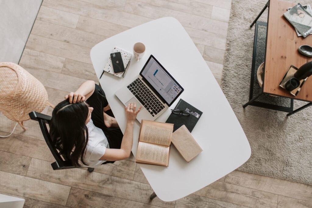 Picture of a birds-eye view of a person sat at a desk with a laptop and books