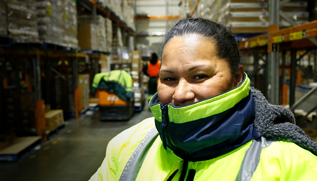 A Woolworths / primary connect employee looking confident and comfortable whilst working in a warehouse - a person is behind her on a picker 