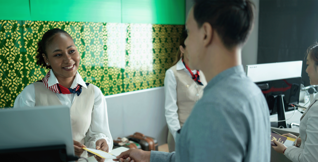 A woman at the counter of a check-in desk serving a male customer